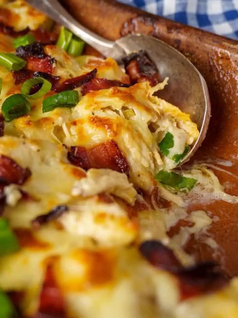 Close-up of a fork lifting a portion of cheesy rotisserie chicken casserole, topped with crispy bacon and fresh green onions, showing the rich, gooey texture.