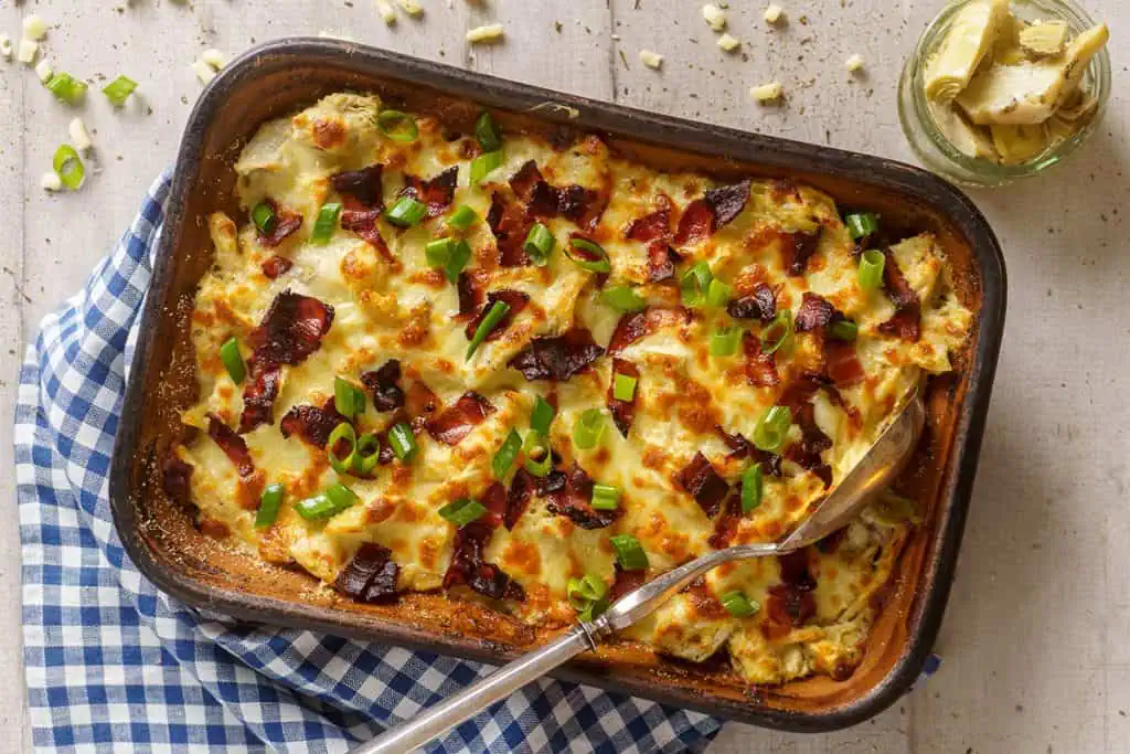 A golden-brown rotisserie chicken casserole fresh out of the oven, with crispy bacon bits and melted cheese on top, garnished with chopped green onions, ready to serve.