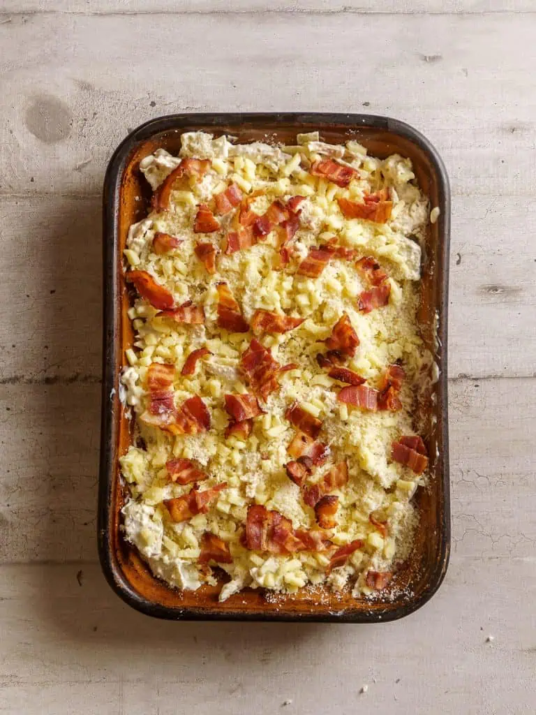 Fully assembled casserole with cheese and bacon, ready for baking.