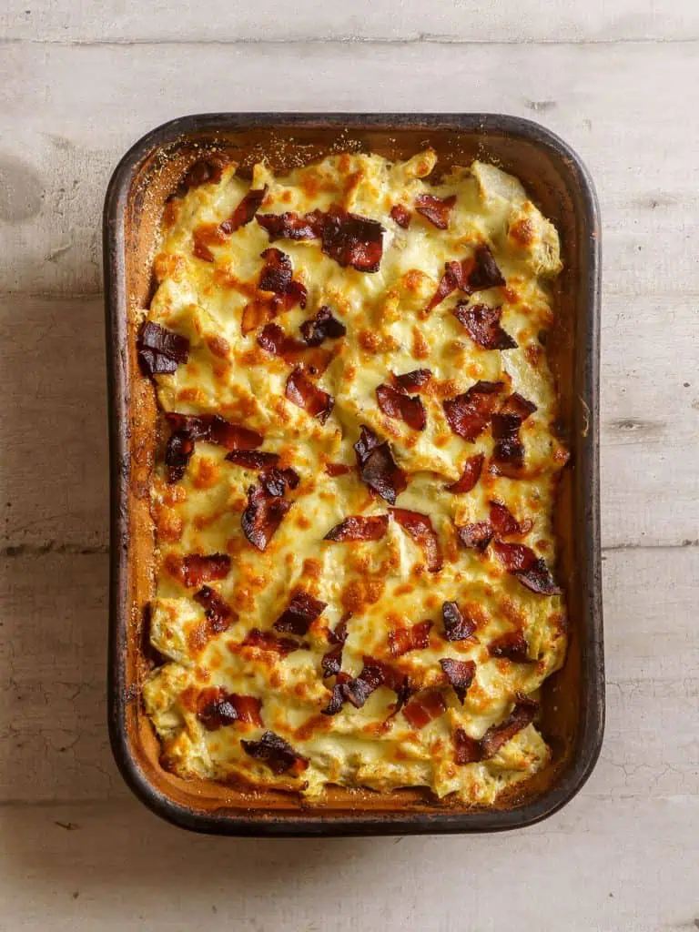 The baked casserole fresh out of the oven, with golden brown melted cheese and crispy bacon on top.