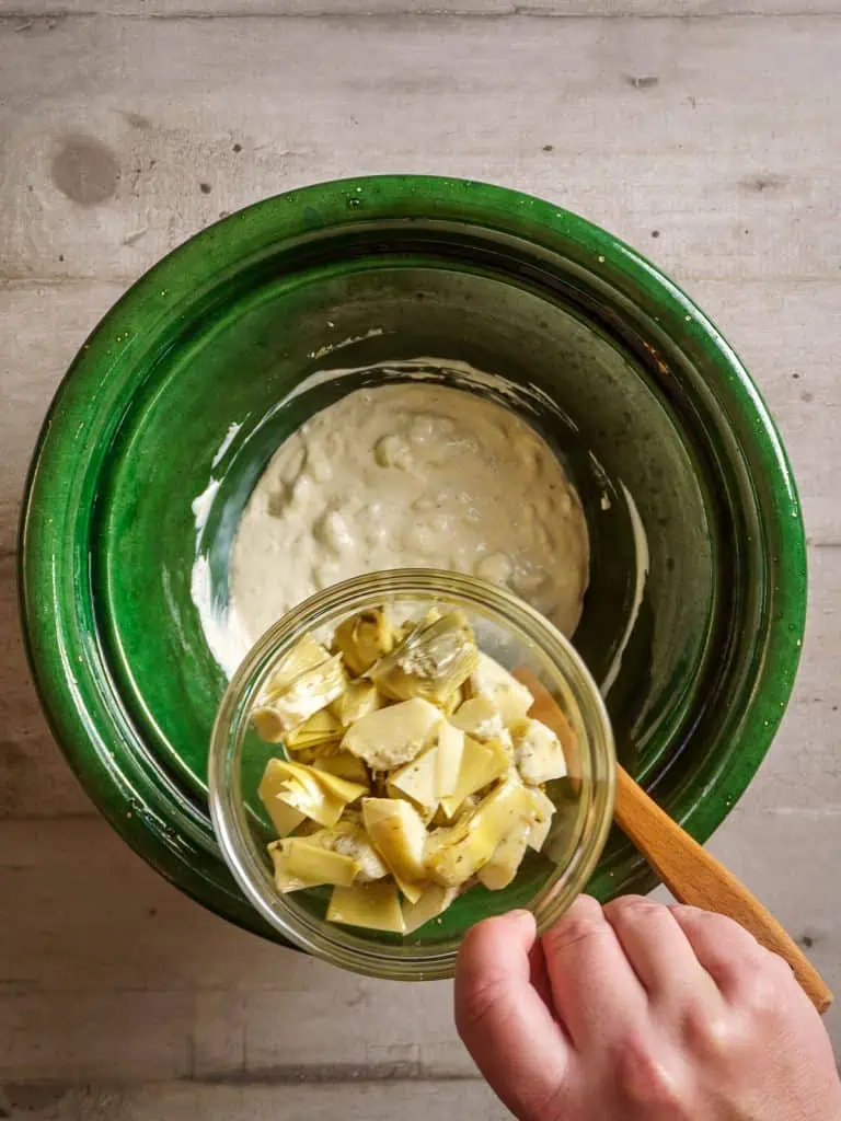 Artichoke hearts being added to the cream mixture in the green bowl.