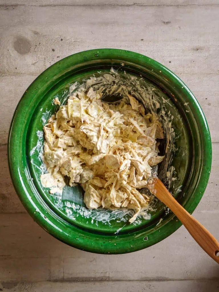Shredded rotisserie chicken added to the cream mixture in the green bowl, ready to be mixed.