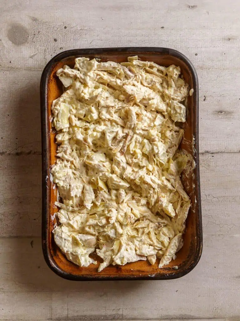 The creamy chicken and artichoke mixture spread evenly in a casserole dish.