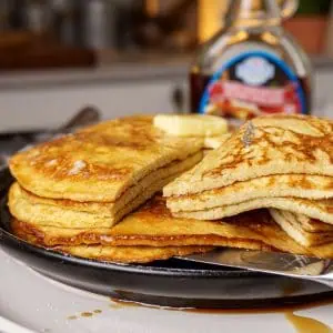 Stack of fluffy, golden-brown cream cheese pancakes with a dollop of butter on top and syrup dripping down the side.