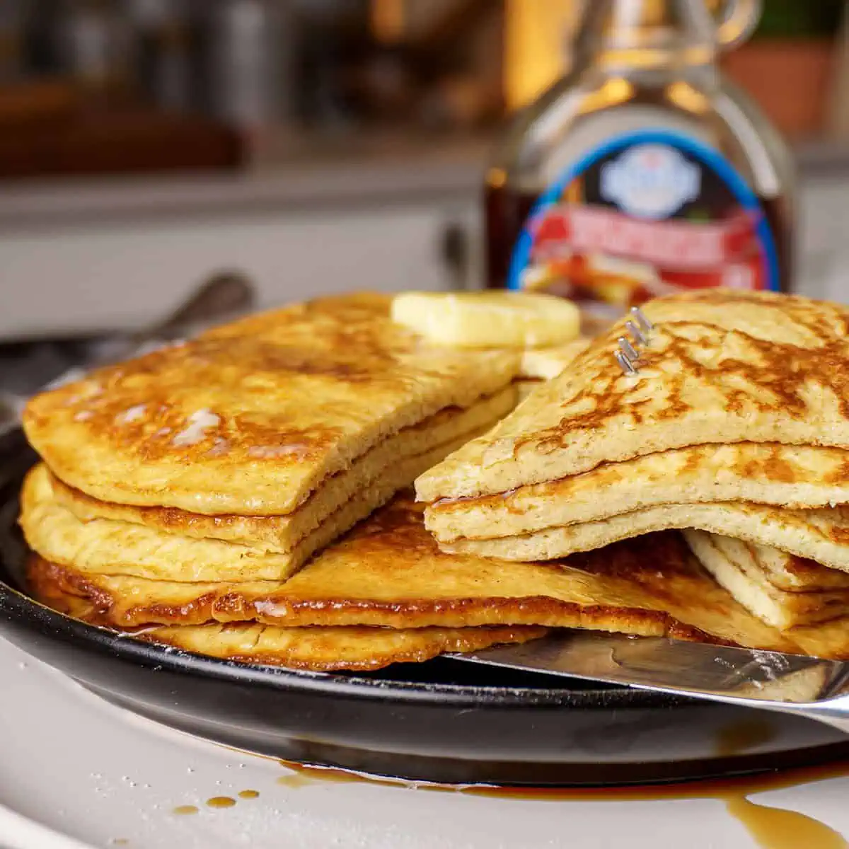 Stack of fluffy, golden-brown cream cheese pancakes with a dollop of butter on top and syrup dripping down the side.