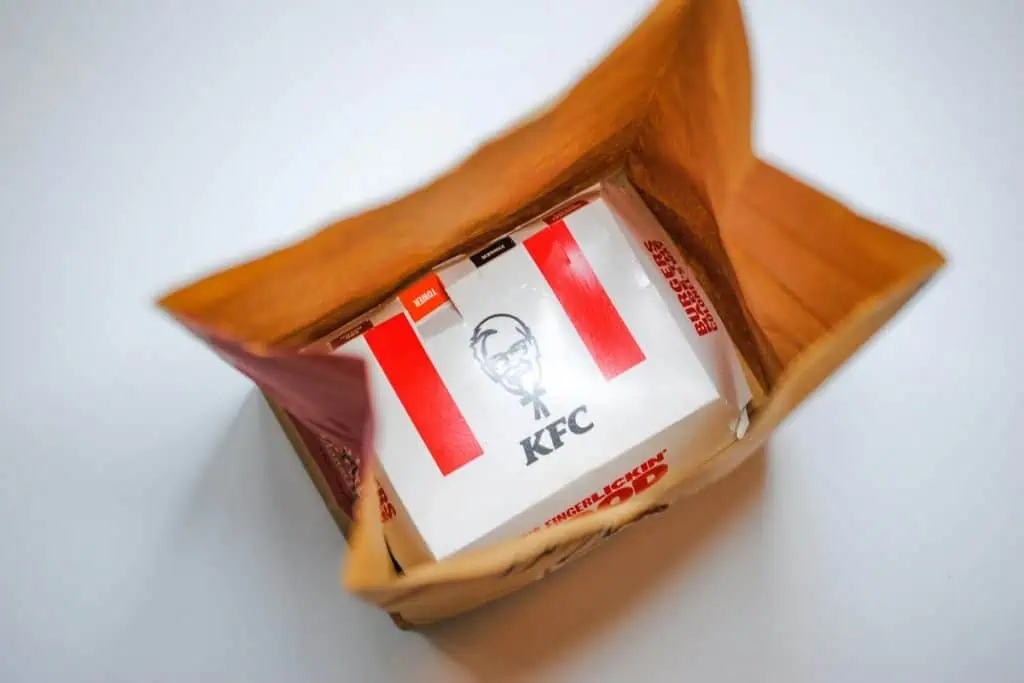 Overhead view of a KFC takeout bag with a boxed meal visible inside, featuring KFC's iconic branding.