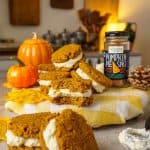 Pumpkin whoopie pies arranged in a fall-themed setting, showcasing the fluffy cream cheese filling and rich pumpkin cookies.