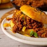 A low-carb sloppy joe served on a golden keto bun with melted cheese and chopped green onions. The filling is overflowing with saucy ground meat, providing a hearty, flavorful meal.