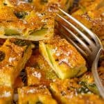 Overhead shot of a sliced zucchini egg bake served on a wooden cutting board with a knife nearby, showcasing a golden-brown crust and scattered zucchini pieces.