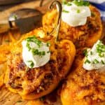 Three stuffed bell peppers filled with shredded chicken and cheese, garnished with sour cream and fresh chives, served on a rustic wooden board.
