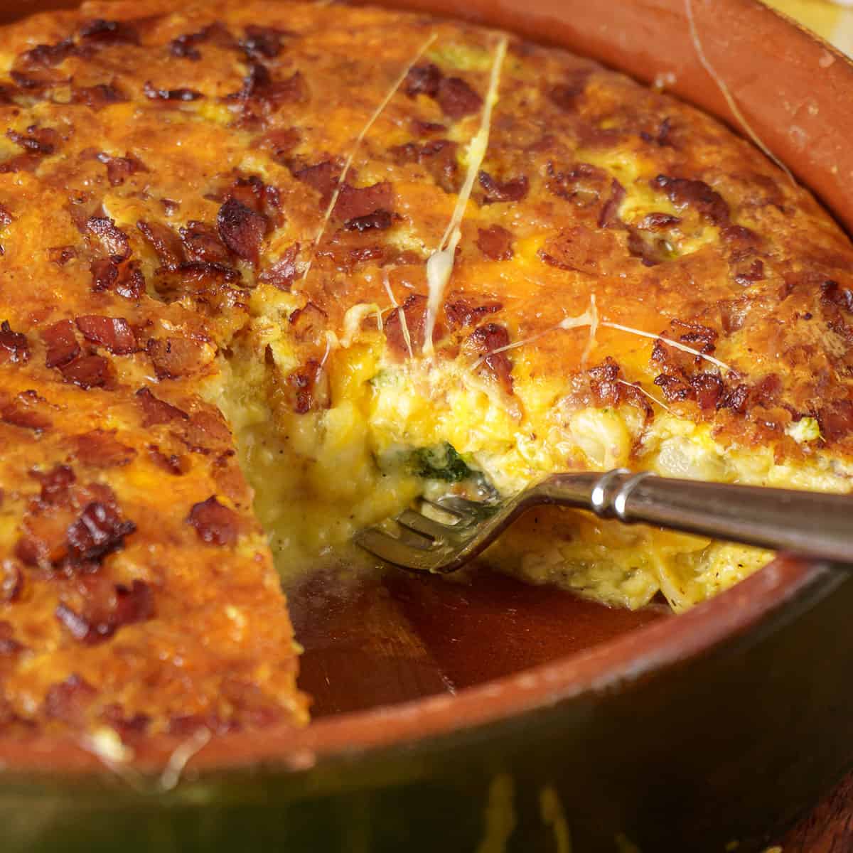 A baked breakfast casserole in a green ceramic dish, topped with melted cheese and crispy bacon, served on a wooden surface.