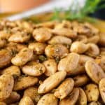 Roasted almonds seasoned with herbs, beautifully arranged in a rustic terracotta bowl, surrounded by rosemary sprigs.