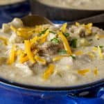 Close-up view of a bowl filled with creamy turkey chowder, topped with shredded cheddar cheese and chopped chives, showcasing hearty chunks of turkey and vegetables in a rich, savory broth.