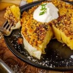 A plated roasted cabbage steak with a golden, cheesy topping. A fork rests on the plate, showing the texture of the caramelized edges.