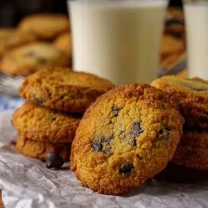 Golden brown keto chocolate chip cookies stacked on parchment paper with a rustic wooden surface underneath.