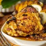 Beautifully charred lemon pepper chicken thighs arranged on a rustic white platter with fresh lemons and black pepper scattered around.