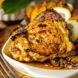 Beautifully charred lemon pepper chicken thighs arranged on a rustic white platter with fresh lemons and black pepper scattered around.