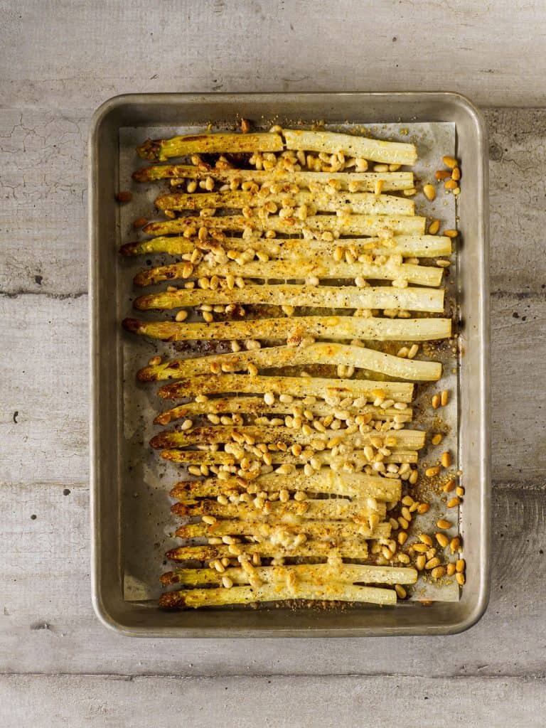 Roasted white asparagus fresh from the oven, golden brown with melted cheese and toasted pine nuts.